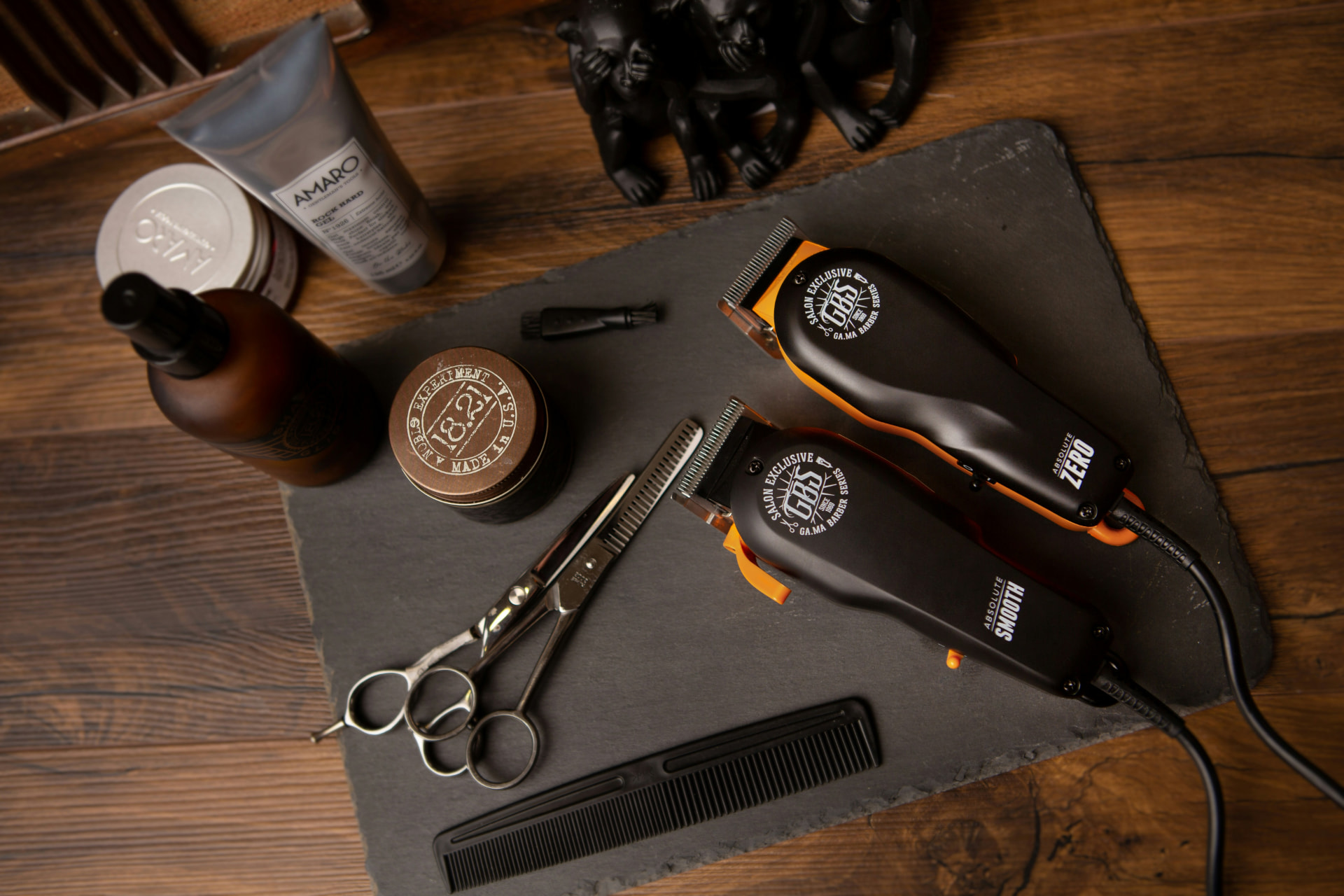 Barber clippers, shears, comb, and grooming products laid out on a slate board
